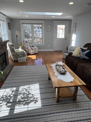 A spacious living room with a fireplace, a large window, and a patterned rug.