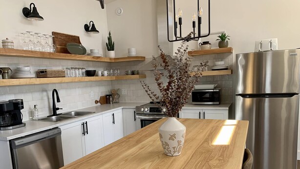 Una cocina moderna con armarios blancos, encimera de madera, refrigerador de acero inoxidable y un jarrón con flores secas.