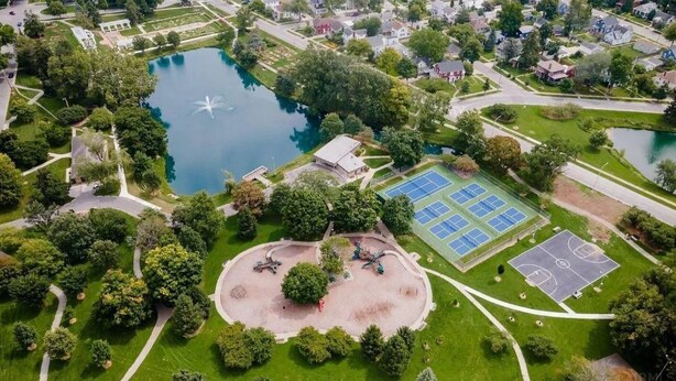 Luchtbeeld van een park met een tennisbaan, een basketbalveld en een vijver.