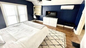 Een slaapkamer met een bed, een plafondventilator, een televisie, een dressoir en een raam met jaloezieën.