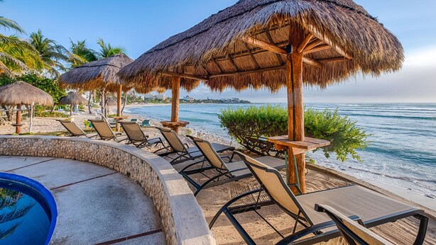 Un complexe hôtelier situé en bord de mer, doté de parasols en chaume, de chaises longues et d’une piscine.