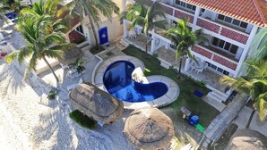Un complexe hôtelier doté d’une piscine, de palmiers et d’un bâtiment surmonté d’un toit recouvert de tuiles rouges.