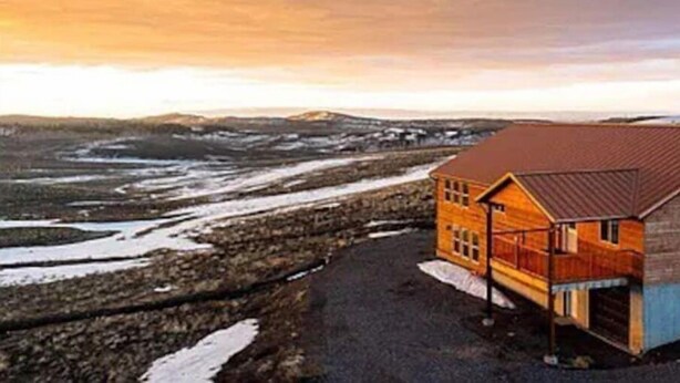 A wooden cabin with a metal roof, situated on a gravel path with snow patches, overlooking a hilly landscape. - Fishlake family cabin! (Sevier County)