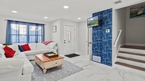 Uma sala de estar moderna com um sofá branco, uma mesa de centro de madeira e uma porta azul com papel de parede náutico.
