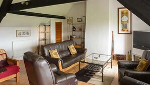A cozy living room with a brown leather sofa, a glass coffee table, and a television. - Gulls Hatch (Maryport)