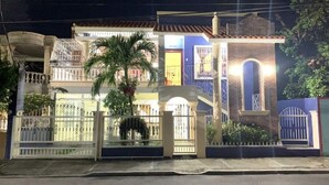 Una casa de dos pisos amb entrada tancada per reixa, un balcó i una palmera al jardí davanter.