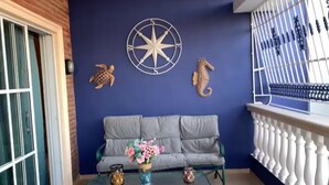 Un balcó amb un sofà gris, una decoració de brúixola estel·lar i dues decoracions de cavall de mar.