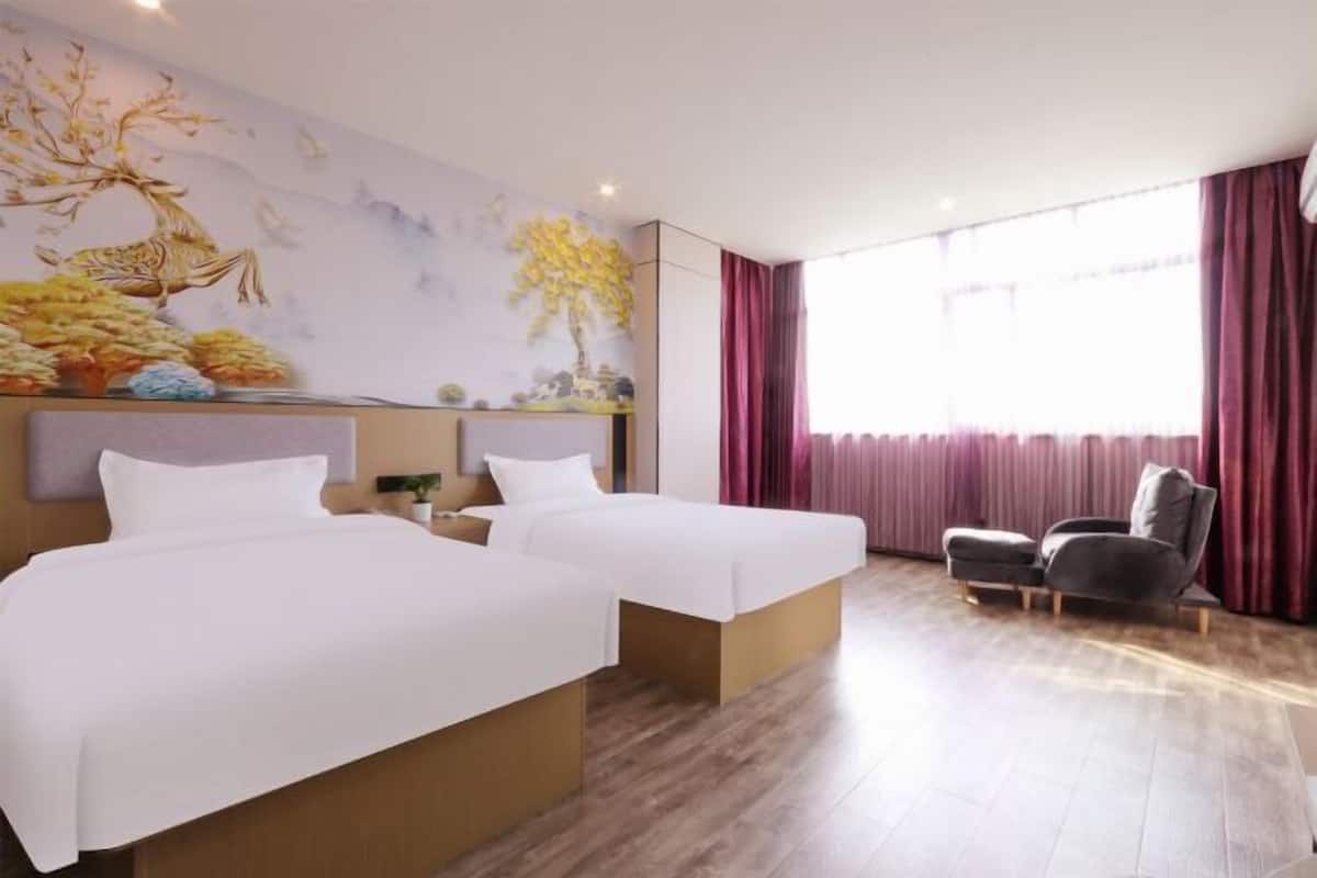 A hotel room with two beds, a chair, a large window with curtains, and a mural on the wall.