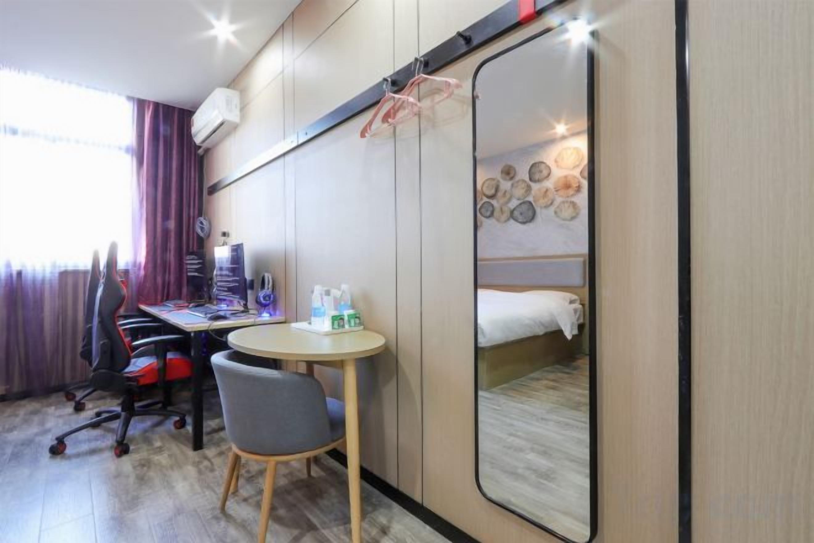 Quarto de hotel com cama, escrivaninha com computador, cadeira e pequena mesa com produtos de higiene pessoal.