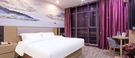 A hotel room with a large bed, a desk with a chair, a small table with a vase of flowers, and a large window with purple curtains.