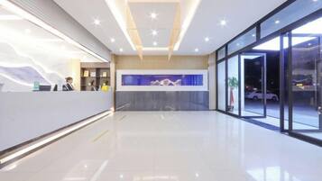 A modern hotel reception area with a clean, minimalist design, a reception desk, and a large glass window offering a view of the outside.