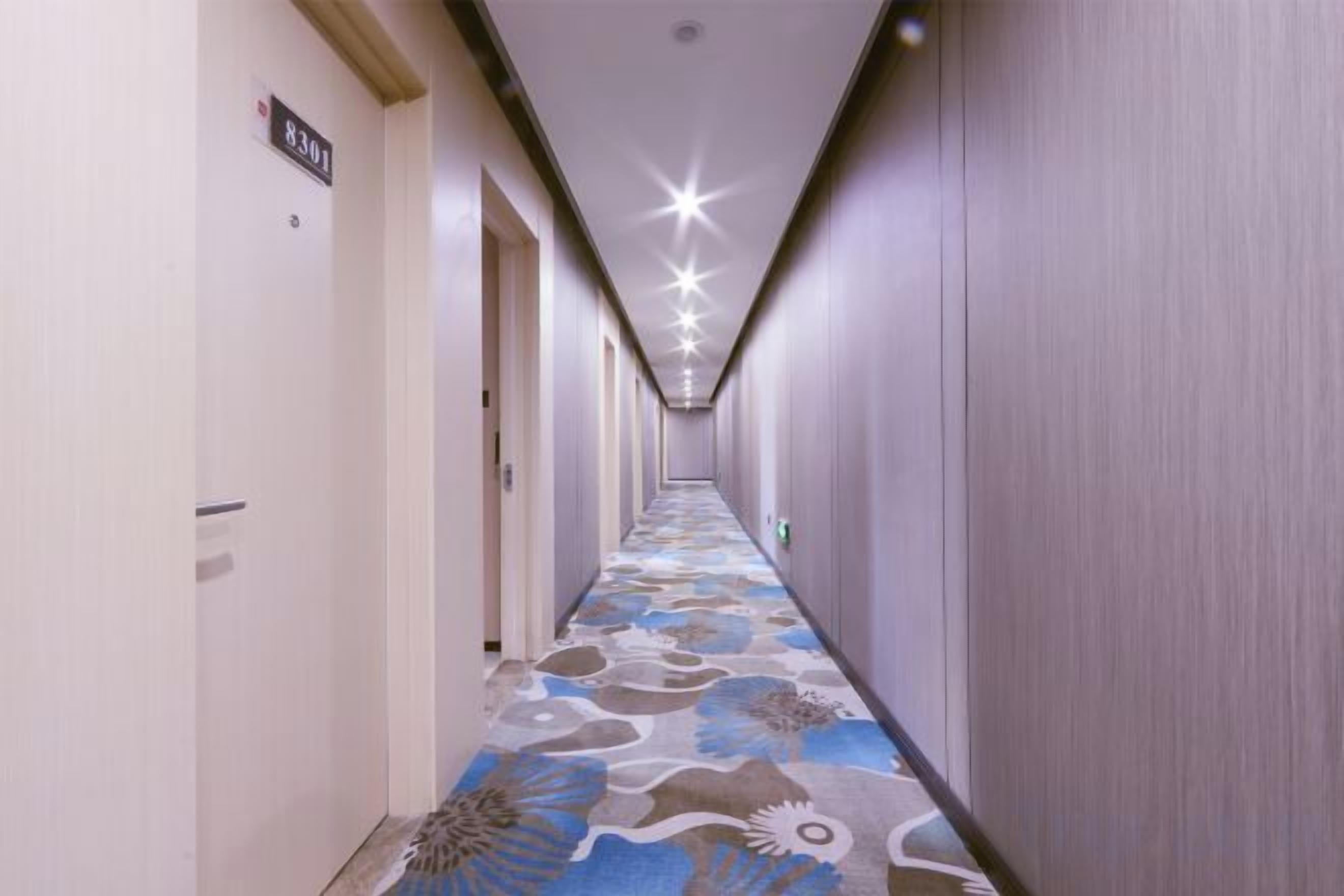 A hotel corridor with a patterned carpet, doors on the left, and a sign indicating room number 8301.