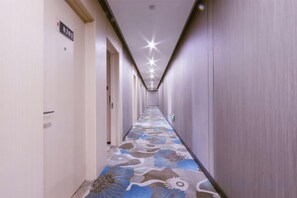 Een hotelgang met een kamergestreept tapijt, deuren aan de linkerkant en een bordje met het kamernummer 8301.