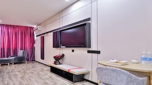 A modern hotel room with a large flat-screen TV mounted on the wall, a bench, a desk with a chair, and a window with curtains. - Shankee Hotel (Wujiang Pedestrian Street) (Suzhou)