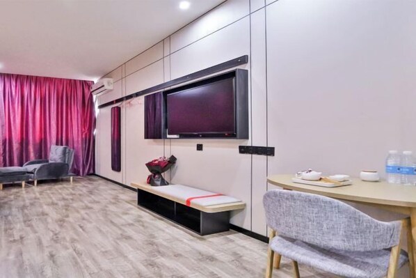 A modern hotel room with a large flat-screen TV mounted on the wall, a bench, a desk with a chair, and a window with curtains. - Shankee Hotel (Wujiang Pedestrian Street) (Suzhou)