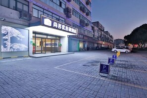 A hotel entrance with a sign, a parking area, and a building in the background.