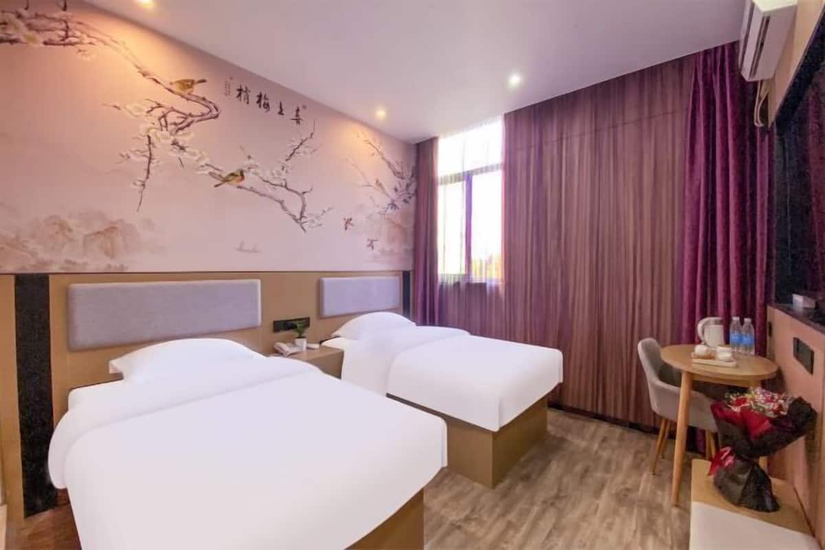 A hotel room with two beds, a desk, a chair, and a decorative wall with artwork.