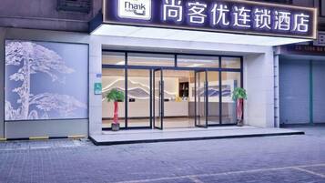 A hotel entrance with a glass facade, a wheelchair accessibility sign, and two potted plants.