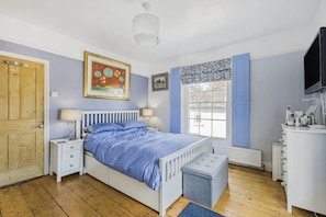 Une chambre à coucher comprenant un lit, des tables de chevet, une fenêtre avec des rideaux, un radiateur et un téléviseur.