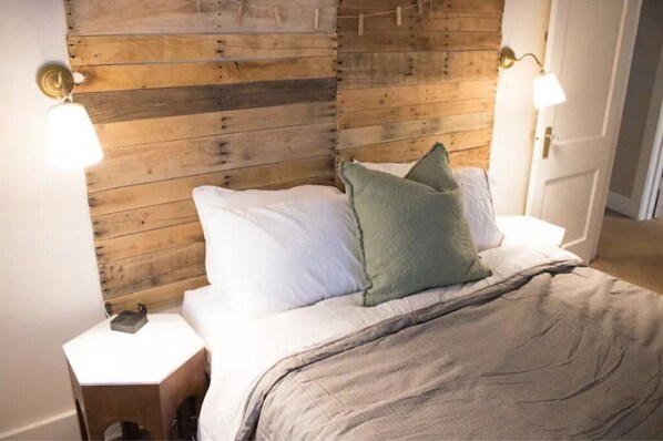 A bedroom with a wooden headboard, a bed with white and green pillows, and bedside lamps.
