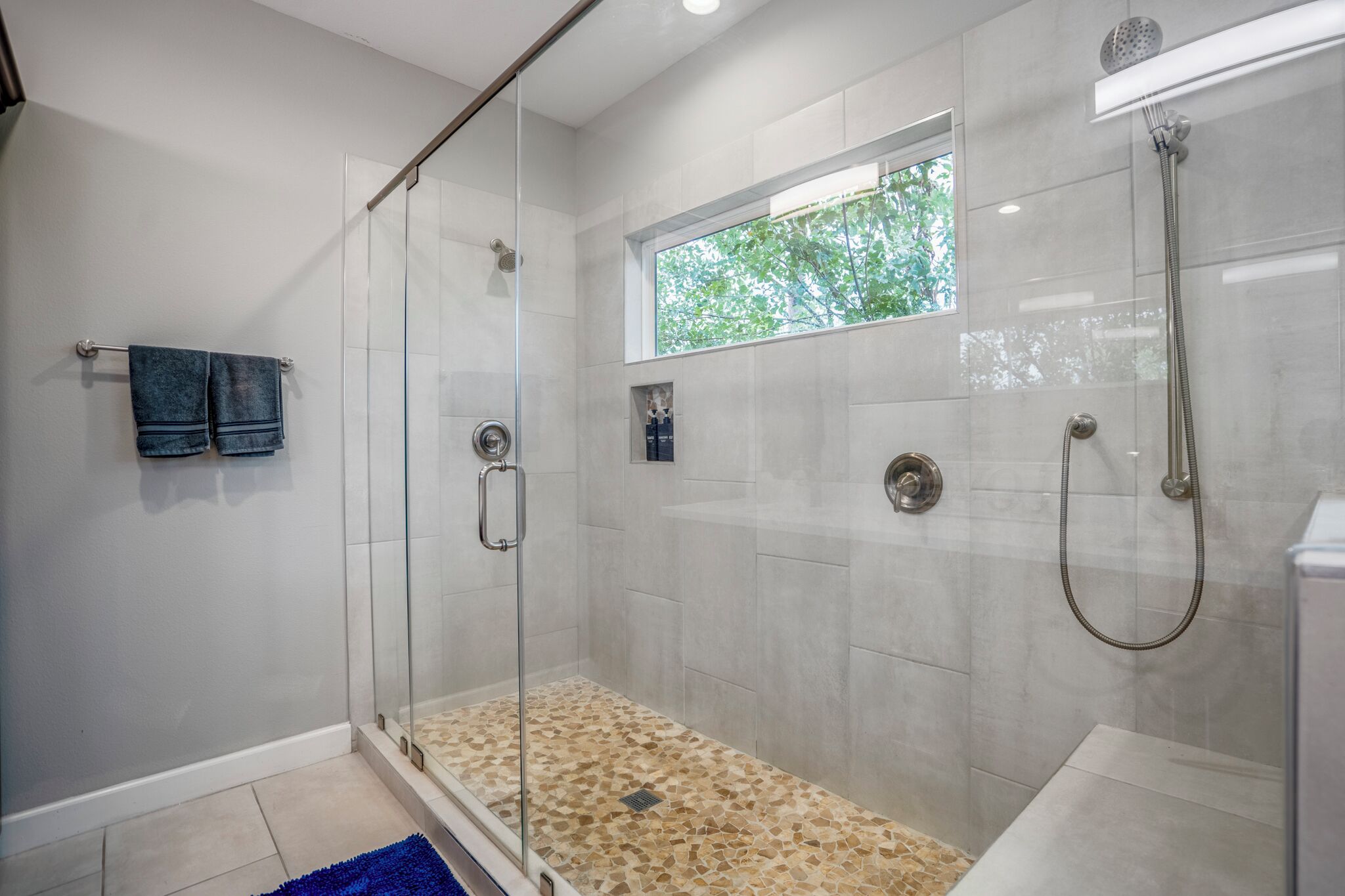 Un baño moderno con ducha de vidrio, ventana y piso de baldosas.