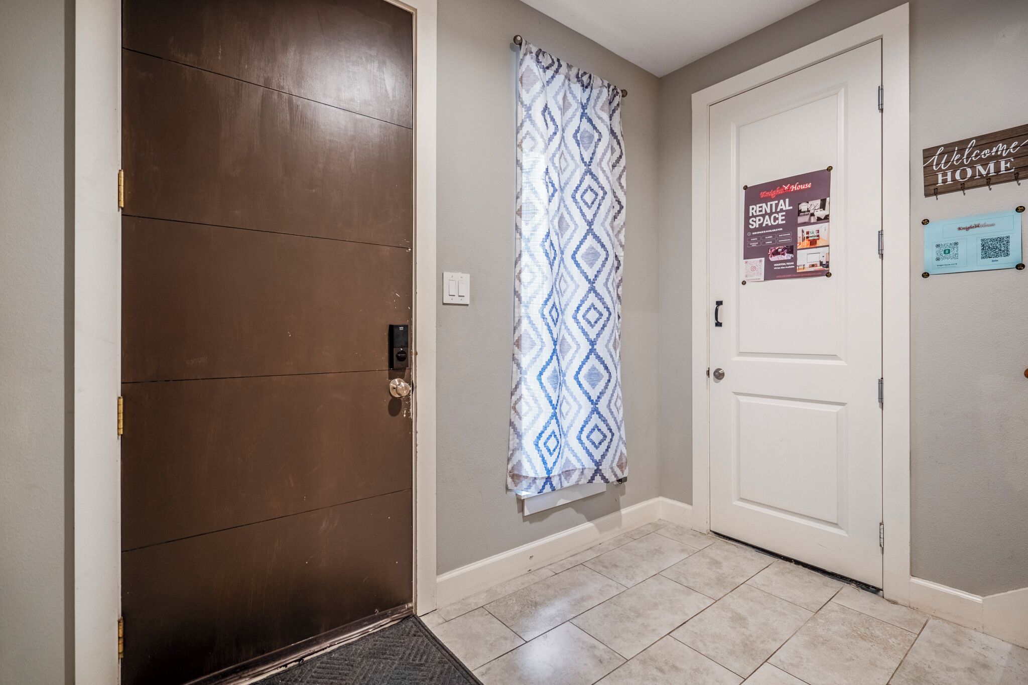 A hallway with a brown door, a patterned curtain, and a door with a 'Welcome Home' sign and a rental space poster.