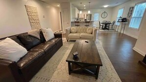 A living room with a dark brown leather sofa, a beige sectional sofa, and a wooden coffee table. There is a patterned rug on the floor. - Cheerful Three-Bedroom Residential Home (Richmond)