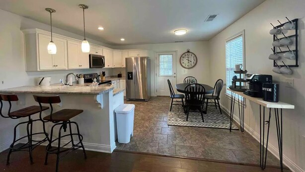 A modern kitchen with white cabinets, stainless steel appliances, and a dining area with a round table and chairs. - Cheerful Three-Bedroom Residential Home (Richmond)