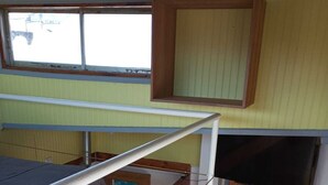 Une chambre avec un lit superposé, une fenêtre, une porte et un escalier.