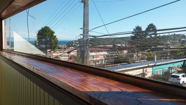 Une vue à travers une fenêtre à cadre en bois, donnant sur un quartier résidentiel avec des maisons, une route et une étendue d’eau.