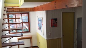 Une pièce compacte avec un lit superposé, un escalier en bois, une petite table et une fenêtre donnant sur des immeubles.