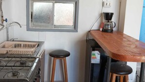 Une cuisine équipée d’une cuisinière à gaz, de tabourets en bois, d’une machine à café et d’un tableau représentant des personnes accroché au mur.