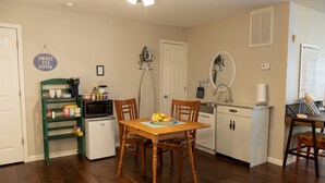 A compact kitchen with a dining table, chairs, a refrigerator, a microwave, and a coffee station.