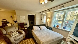A bedroom with a bed, a sofa, a desk, and a window with a view of the outside.