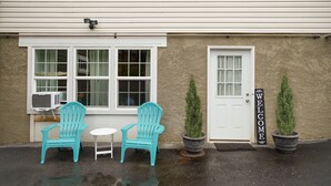 A building with a white exterior, a white door, and a welcome sign. There are two turquoise chairs and a small table outside.