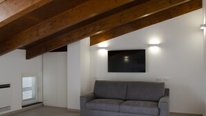 Una sala de estar moderna con un sofá gris, vigas de madera, un televisor de pantalla plana e iluminación empotrada.