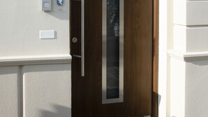 Puerta de madera con un panel de vidrio vertical, timbre y buzón.