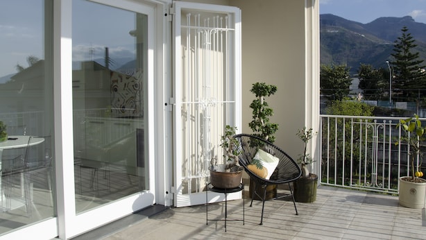 Un balcón con puerta de cristal, una mesa con sillas y plantas en macetas.