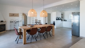 A modern kitchen with a wooden dining table and chairs, a stainless steel refrigerator, and pendant lights.