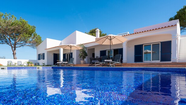 A modern house with a swimming pool, outdoor seating, and a clear blue sky.