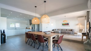 A modern kitchen with a wooden dining table and chairs, pendant lights, and a large window.