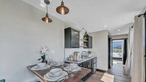 Een moderne keuken met een eethoek, met een houten tafel gedekt voor zes personen, een inbouwoven en uitzicht naar buiten.