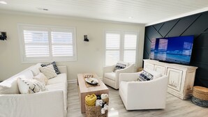 Uma sala de estar moderna com um sofá branco, uma mesa de centro e uma televisão de tela plana em uma parede de destaque preta.