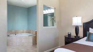A hotel room with a large bed, a nightstand with a lamp, a bathroom with a bathtub and a mirror. - 1BD/Williamsburg at Governor's Green - Lots to do! (Williamsburg)