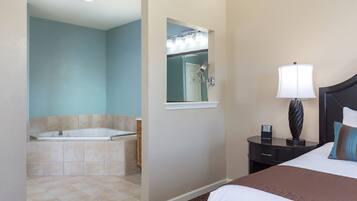 Une chambre d’hôtel avec un grand lit, une table de chevet avec une lampe, une salle de bain avec une baignoire et un miroir.