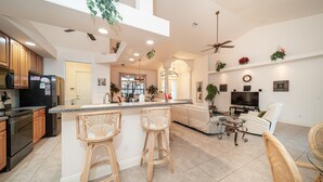 A spacious kitchen with a large island, bar stools, and a dining area with a TV and seating. - Villa Sunset with heated Pool and Privacy on the canal (Cape Coral)