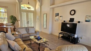 A living room with a sofa, armchairs, a coffee table, a TV, and a fireplace. - Villa Sunset with heated Pool and Privacy on the canal (Cape Coral)