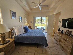 Une chambre avec un lit, une commode, un ventilateur de plafond et une vue sur une piscine et un espace de détente extérieur.
