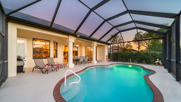 An indoor swimming pool with a glass ceiling, lounge chairs, and a patio area. - Villa Sunset with heated Pool and Privacy on the canal (Cape Coral)