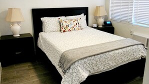 Un dormitorio con una cama, dos mesitas de noche con lámparas, un ventilador de techo y una ventana con persianas.